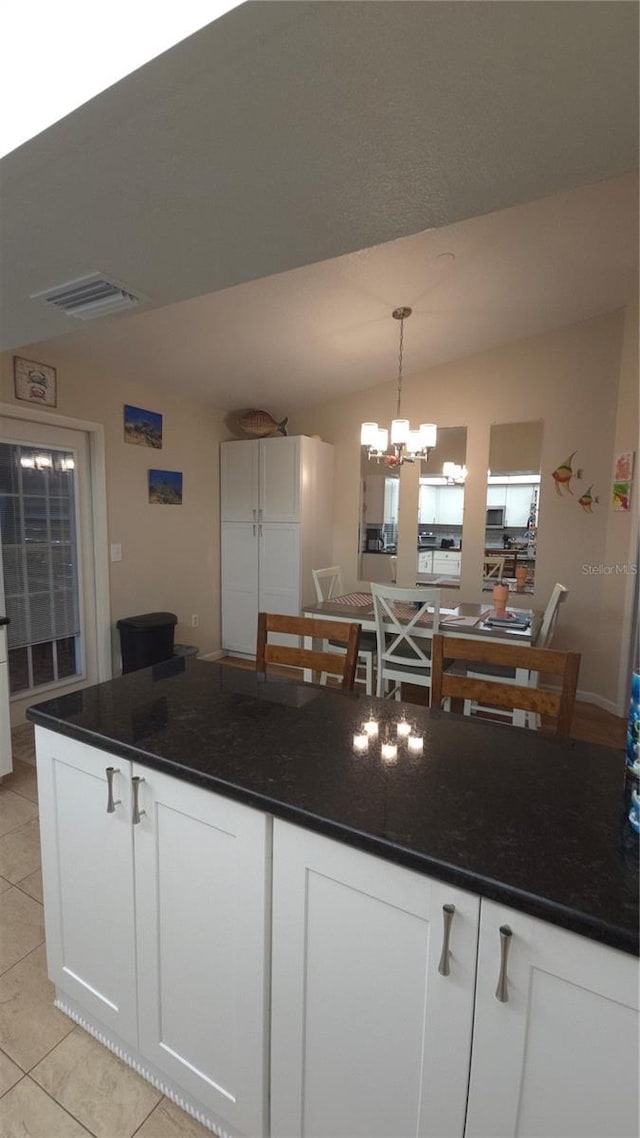 kitchen featuring white cabinetry, decorative light fixtures, vaulted ceiling, and dark stone countertops