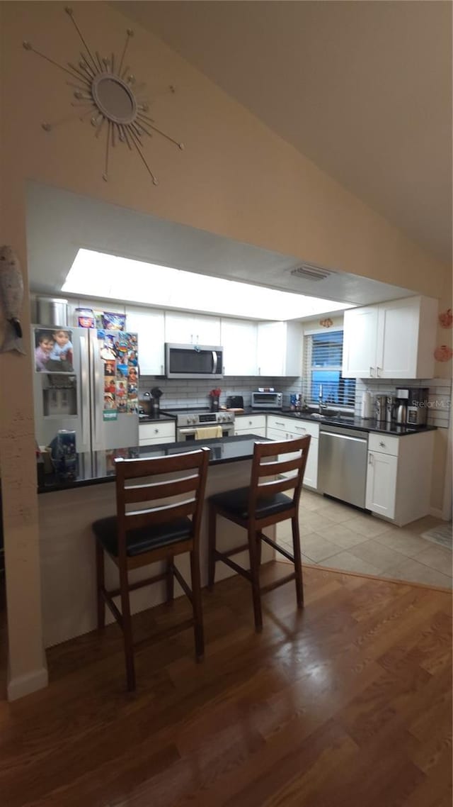 kitchen with a breakfast bar area, stainless steel appliances, tasteful backsplash, white cabinets, and light wood-type flooring