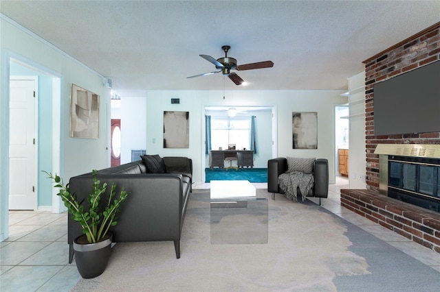 living room featuring ceiling fan, a brick fireplace, a textured ceiling, and light tile patterned floors