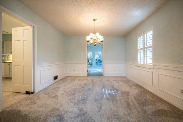 unfurnished dining area featuring light carpet, a textured ceiling, and a chandelier