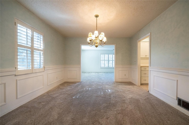 unfurnished dining area featuring light carpet, a textured ceiling, and an inviting chandelier