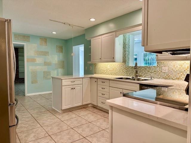 kitchen with sink, white cabinets, kitchen peninsula, and stainless steel refrigerator