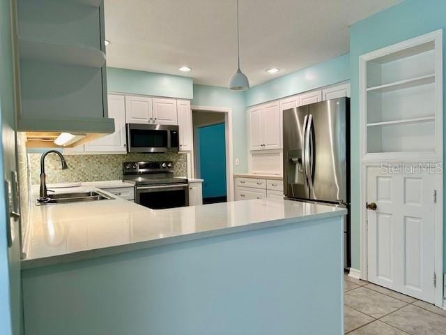 kitchen featuring decorative light fixtures, sink, white cabinets, kitchen peninsula, and stainless steel appliances