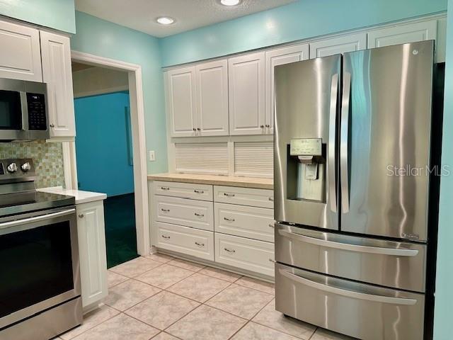 kitchen featuring tasteful backsplash, stainless steel appliances, light tile patterned floors, and white cabinets