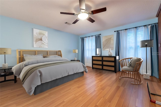 bedroom with a textured ceiling, ceiling fan, and light hardwood / wood-style flooring