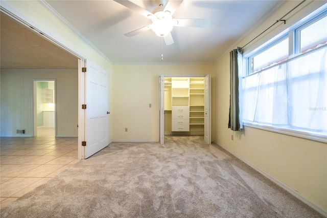 unfurnished bedroom featuring crown molding, a spacious closet, light carpet, a closet, and ceiling fan