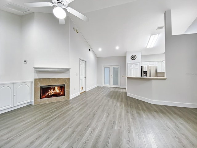 unfurnished living room featuring ceiling fan, a tiled fireplace, light wood-type flooring, and high vaulted ceiling