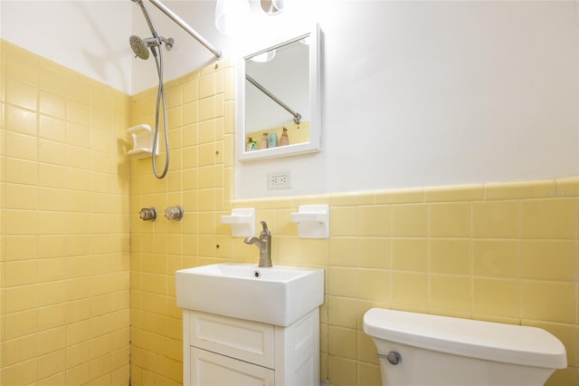 bathroom with tile walls, toilet, vanity, and a tile shower