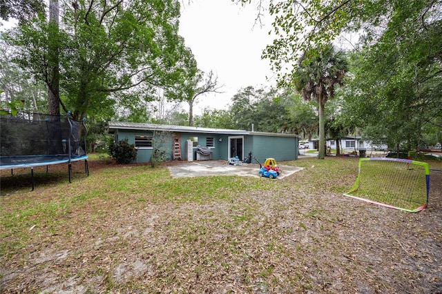 back of property with a trampoline, a lawn, and a patio