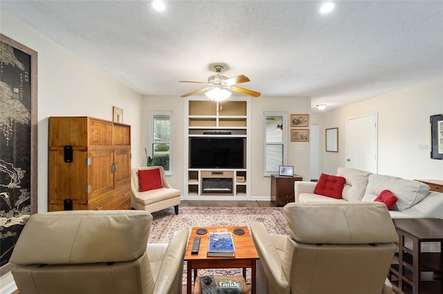 living room featuring ceiling fan, built in shelves, a textured ceiling, and hardwood / wood-style floors