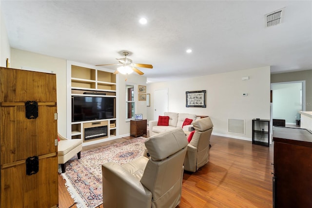 living room featuring ceiling fan, built in shelves, and hardwood / wood-style floors