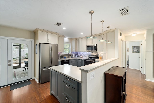 kitchen with kitchen peninsula, appliances with stainless steel finishes, gray cabinetry, tasteful backsplash, and hanging light fixtures