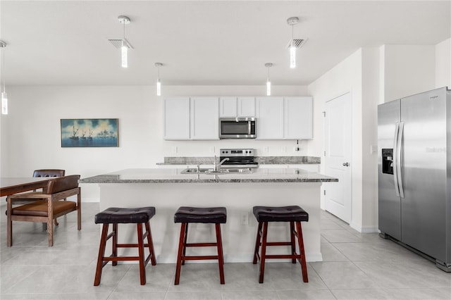 kitchen with hanging light fixtures, white cabinets, stainless steel appliances, and a center island with sink