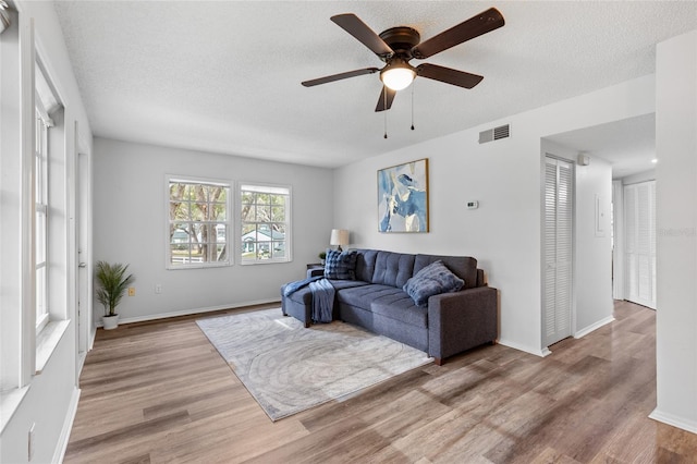 living room with a textured ceiling, ceiling fan, and light hardwood / wood-style floors