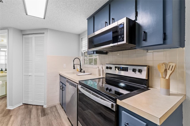 kitchen featuring light hardwood / wood-style floors, appliances with stainless steel finishes, decorative backsplash, blue cabinetry, and sink