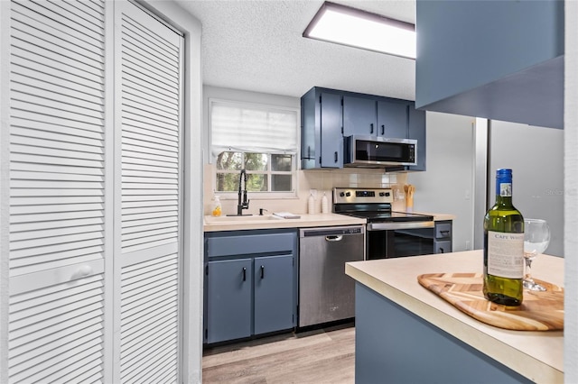 kitchen featuring a textured ceiling, stainless steel appliances, sink, backsplash, and blue cabinets