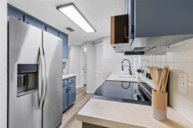 kitchen featuring stainless steel refrigerator with ice dispenser, blue cabinets, a textured ceiling, light hardwood / wood-style flooring, and sink