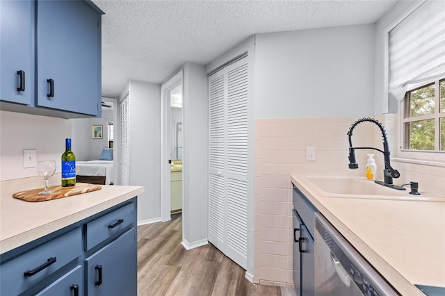 kitchen featuring light hardwood / wood-style floors, blue cabinetry, dishwasher, a textured ceiling, and sink