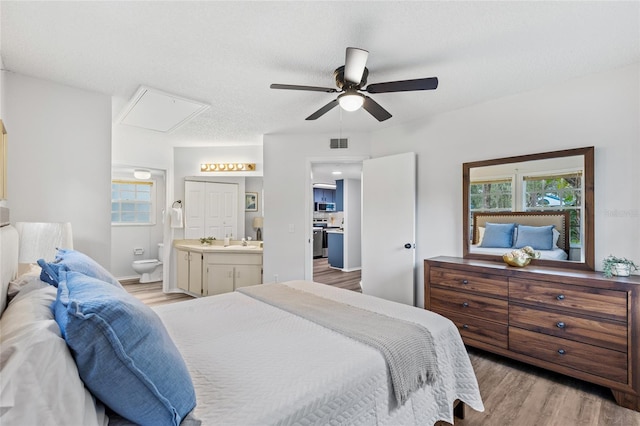 bedroom featuring a textured ceiling, ensuite bath, sink, ceiling fan, and light hardwood / wood-style flooring