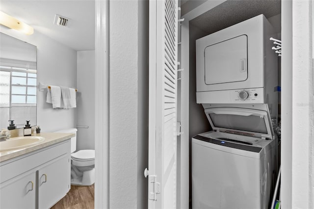 laundry room with sink, stacked washer and clothes dryer, and light hardwood / wood-style flooring