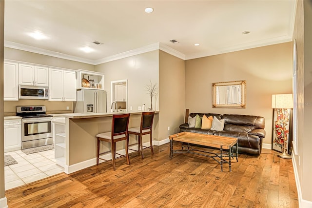 kitchen with a breakfast bar area, white cabinetry, stainless steel appliances, ornamental molding, and light hardwood / wood-style floors