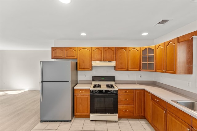 kitchen featuring gas range, sink, light tile patterned floors, and stainless steel refrigerator