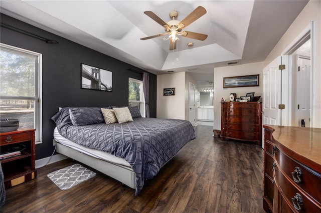 bedroom with multiple windows, dark hardwood / wood-style flooring, ceiling fan, and a tray ceiling