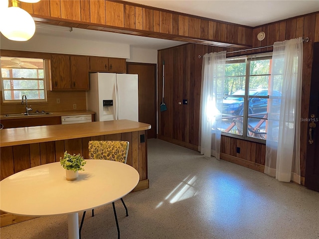 kitchen with sink, backsplash, white fridge with ice dispenser, and wood walls