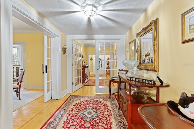 corridor with french doors, ornamental molding, light hardwood / wood-style flooring, and a textured ceiling