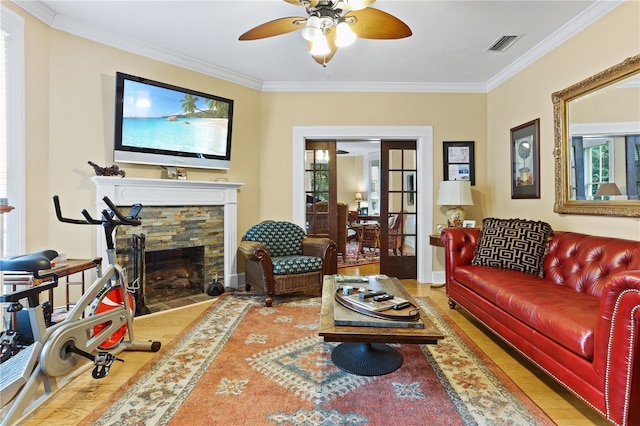 living room featuring ornamental molding, a stone fireplace, ceiling fan, and light wood-type flooring