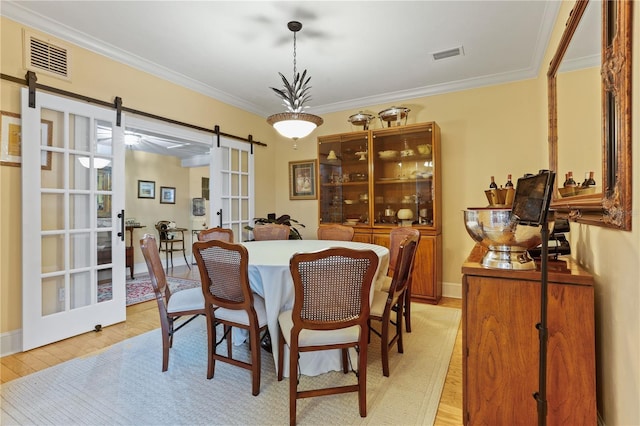 dining space with crown molding, a barn door, and light wood-type flooring