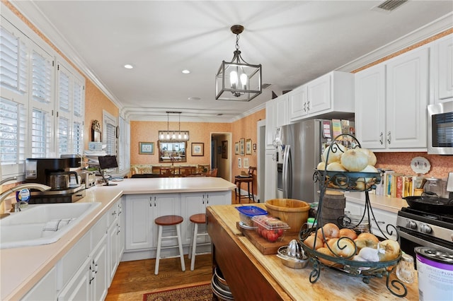 kitchen featuring sink, crown molding, hanging light fixtures, stainless steel appliances, and white cabinets