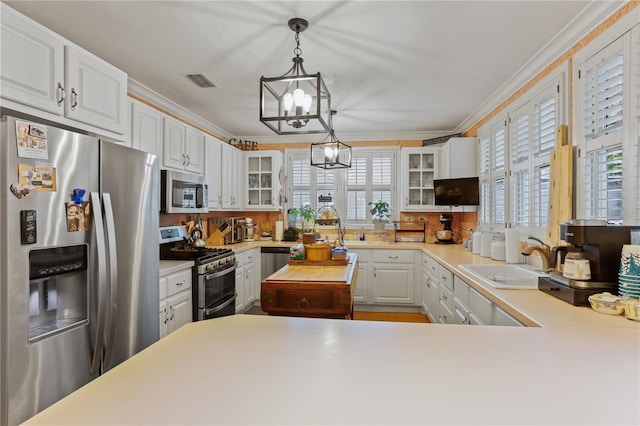 kitchen featuring pendant lighting, sink, appliances with stainless steel finishes, ornamental molding, and white cabinets