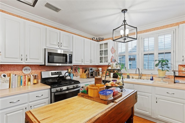 kitchen featuring sink, white cabinetry, hanging light fixtures, ornamental molding, and appliances with stainless steel finishes