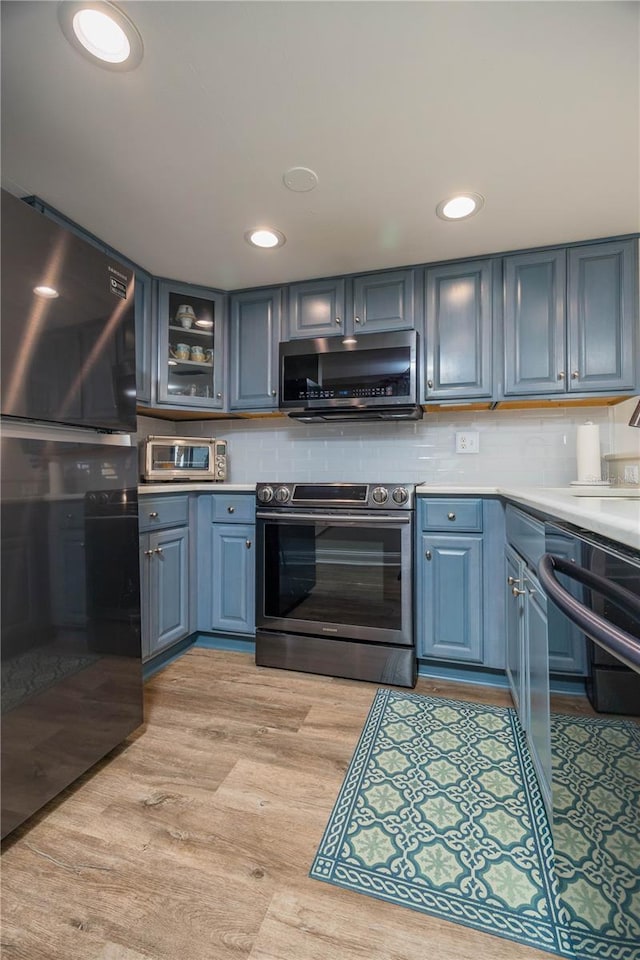 kitchen featuring tasteful backsplash, appliances with stainless steel finishes, blue cabinetry, and light wood-type flooring