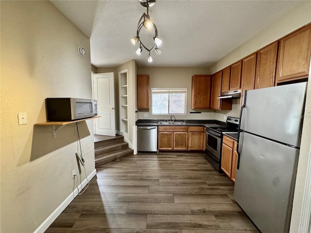 kitchen with appliances with stainless steel finishes, dark hardwood / wood-style floors, sink, hanging light fixtures, and a textured ceiling