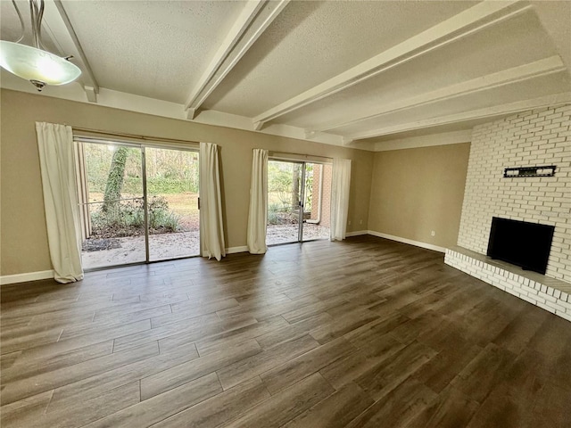 unfurnished living room with beamed ceiling, dark hardwood / wood-style flooring, a brick fireplace, and a textured ceiling