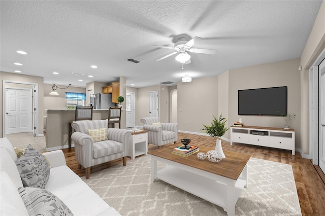 living room featuring ceiling fan, light hardwood / wood-style flooring, and a textured ceiling