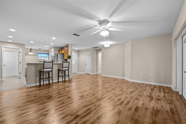 unfurnished living room with a textured ceiling, ceiling fan, and light wood-type flooring