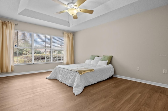 bedroom with hardwood / wood-style flooring, ceiling fan, and a raised ceiling