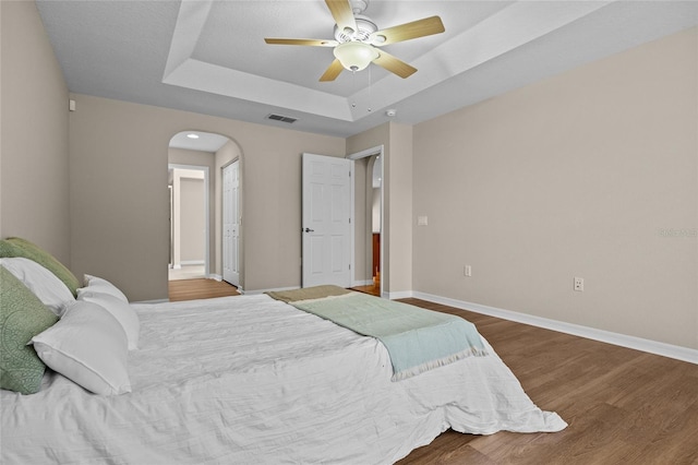 bedroom featuring ceiling fan, wood-type flooring, and a raised ceiling