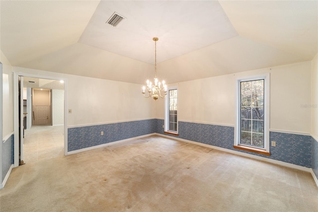 carpeted empty room featuring an inviting chandelier and vaulted ceiling