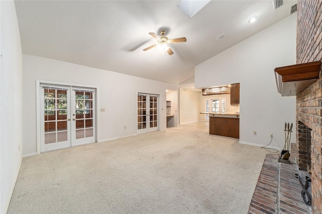 unfurnished living room featuring a fireplace, a skylight, light colored carpet, ceiling fan, and french doors