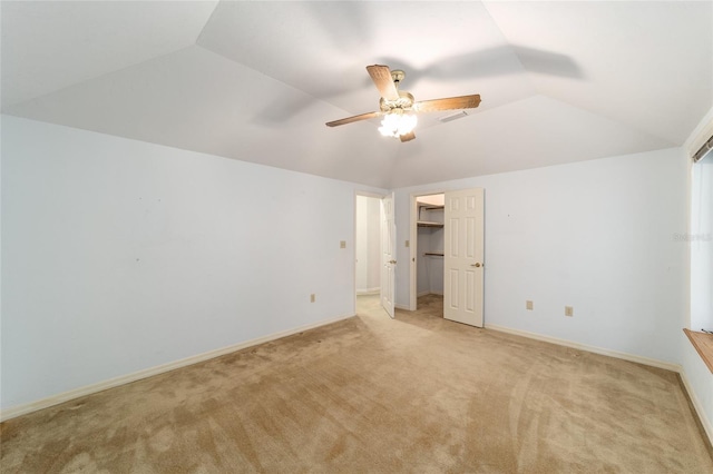 unfurnished bedroom featuring vaulted ceiling, a walk in closet, light carpet, and ceiling fan