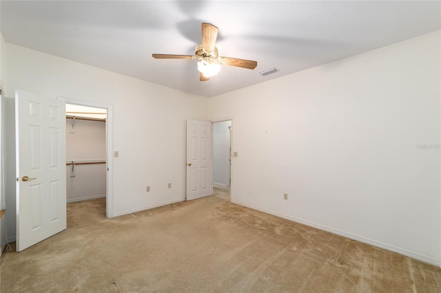 unfurnished bedroom featuring light carpet, a walk in closet, a closet, and ceiling fan