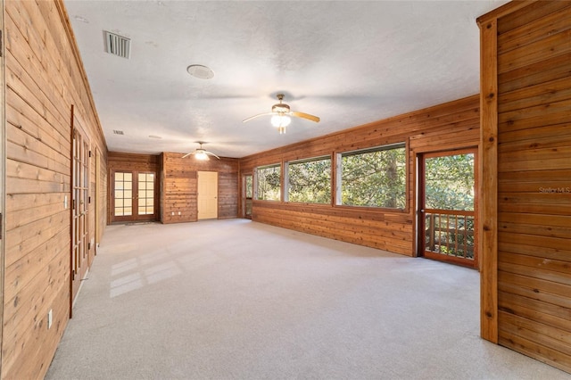 unfurnished living room with ceiling fan, light colored carpet, and wooden walls