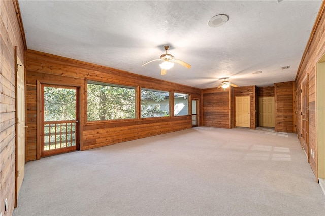 carpeted empty room with ceiling fan, wooden walls, and a textured ceiling