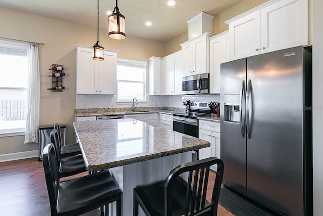 kitchen with appliances with stainless steel finishes, a breakfast bar, pendant lighting, white cabinetry, and a center island