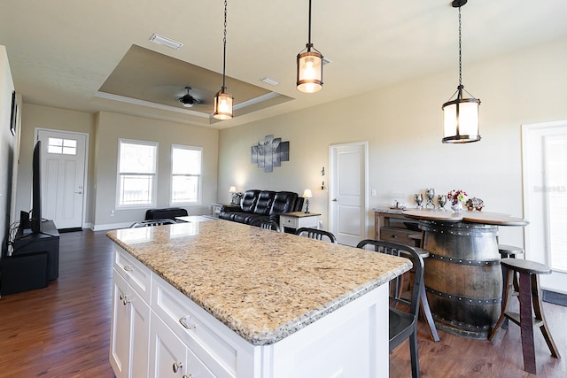 kitchen with white cabinetry, a tray ceiling, hanging light fixtures, and a kitchen island