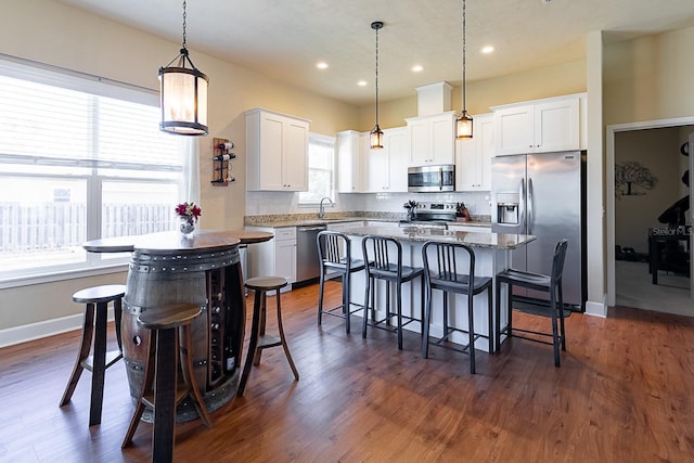 kitchen featuring appliances with stainless steel finishes, white cabinetry, a kitchen island, a kitchen bar, and decorative light fixtures